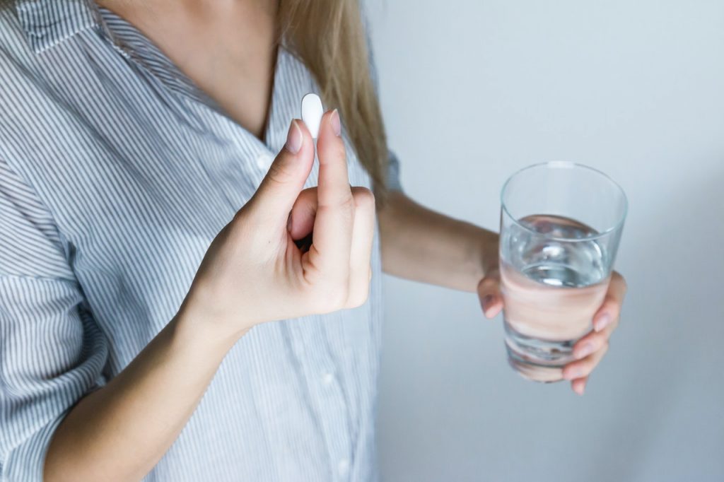 Woman taking medication for pain with glass of water